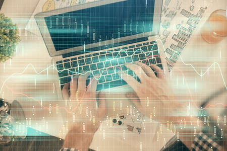 Double exposure of mans hands typing over laptop keyboard and forex chart hologram drawing. Top...