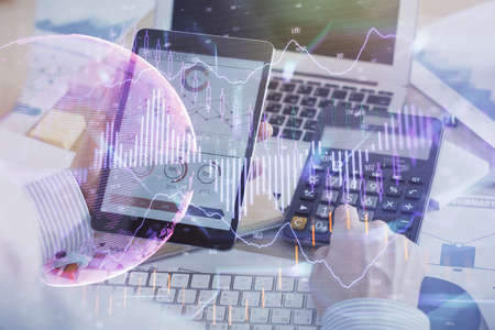 Double exposure of mans hands holding and using a digital device and forex graph drawing. Financial...