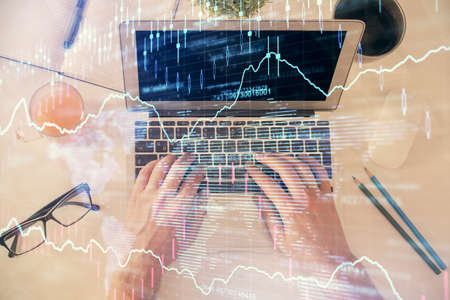 Double exposure of mans hands typing over laptop keyboard and forex chart hologram drawing. Top view. Financial markets concept.の写真素材
