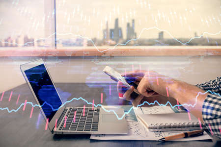 Double exposure of mans hands holding and using a digital device and forex graph drawing. Financial...