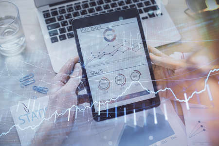 Double exposure of mans hands holding and using a digital device and forex graph drawing. Financial market concept.の写真素材