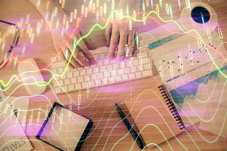 Multi exposure of mans hands typing over computer keyboard and forex graph hologram drawing. Top...