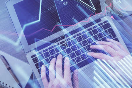 Double exposure of mans hands typing over computer keyboard and forex graph hologram drawing. Top...
