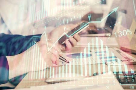 Double exposure of mans hands holding and using a digital device and forex graph drawing. Financial...
