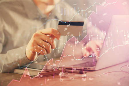 Double exposure of man hands holding a credit card and Forex graph drawing. Stock trading and...