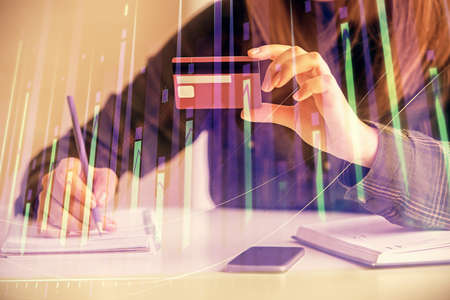 Double exposure of woman on-line shopping holding a credit card and financial graph drawing. Stock market E-commerce concept.の写真素材