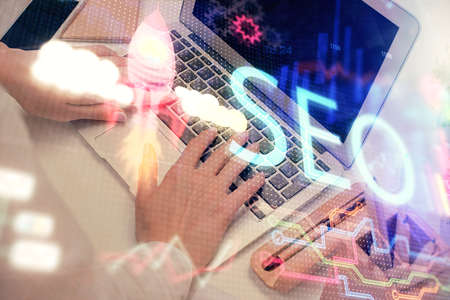 Double exposure of woman hands working on computer and seo hologram drawing. internet search...
