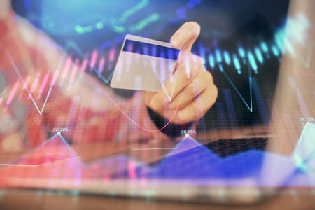 Double exposure of man hands holding a credit card and Forex graph drawing. Stock trading and digital fintech in Internet E-commerce concept.の写真素材