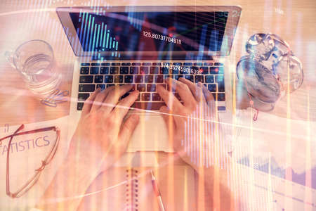 Double exposure of mans hands typing over laptop keyboard and forex chart hologram drawing. Top view. Financial markets concept.の写真素材