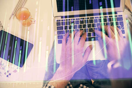 Double exposure of mans hands typing over laptop keyboard and forex chart hologram drawing. Top...