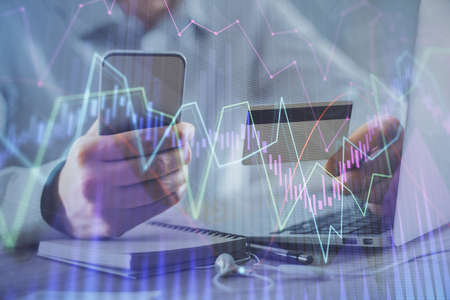 Double exposure of man hands holding a credit card and Forex graph drawing. Stock trading and...