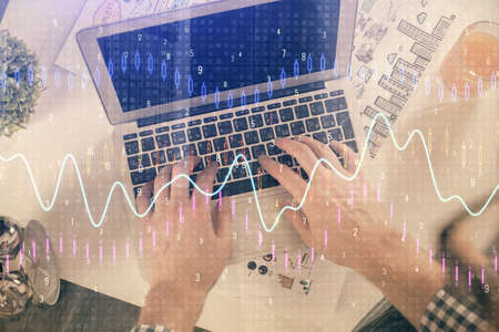 Double exposure of mans hands typing over laptop keyboard and forex chart hologram drawing. Top...