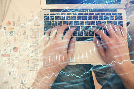 Double exposure of mans hands typing over laptop keyboard and forex chart hologram drawing. Top...