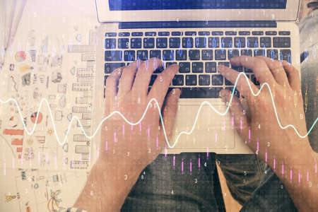 Double exposure of mans hands typing over laptop keyboard and forex chart hologram drawing. Top...