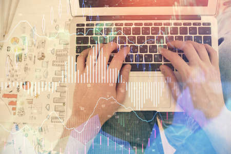 Double exposure of mans hands typing over laptop keyboard and forex chart hologram drawing. Top...