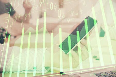 Double exposure of man's hands holding and using a digital device and forex graph drawing. Financial...