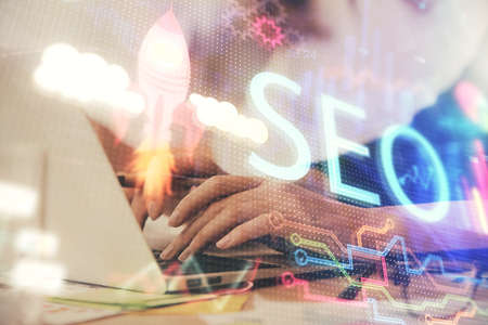 Double exposure of woman hands working on computer and seo hologram drawing. internet search...