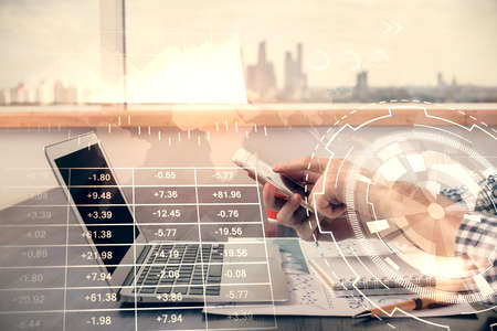 Double exposure of man's hands holding and using a digital device and forex graph drawing. Financial...