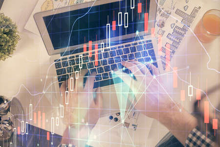 Double exposure of man's hands typing over laptop keyboard and forex chart hologram drawing. Top...