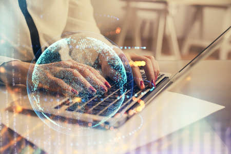 Double exposure of woman hands working on computer and world map hologram drawing. International...