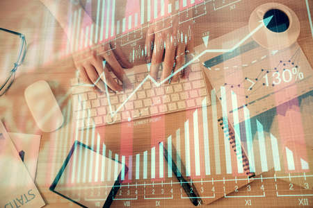 Multi exposure of man's hands typing over computer keyboard and forex graph hologram drawing. Top...