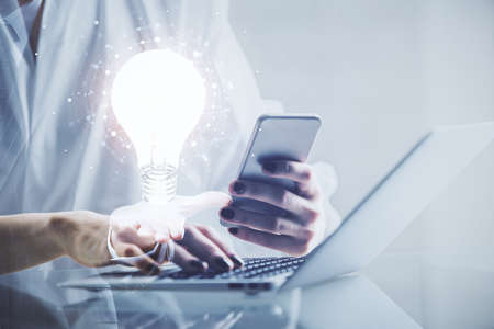 Double exposure of light bulb hologram and woman holding and using a mobile device. Idea concept.の写真素材