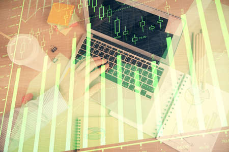 Double exposure of man's hands typing over computer keyboard and forex graph hologram drawing. Top...