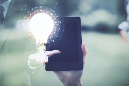 Double exposure of light bulb hologram and woman holding and using a mobile device. Idea concept.の写真素材