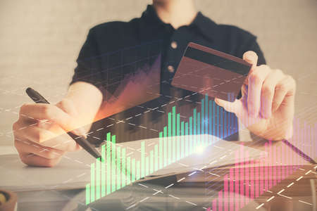 Double exposure of man hands holding a credit card and Forex graph drawing. Stock trading and...