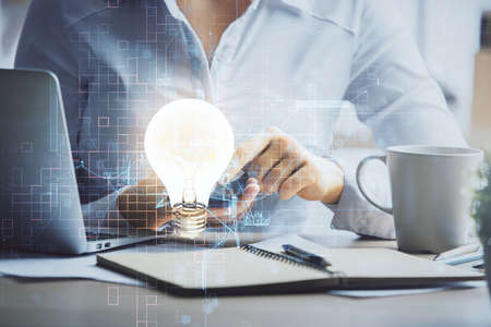 Double exposure of light bulb hologram and woman holding and using a mobile device. Idea concept.の写真素材