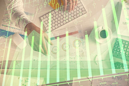 Multi exposure of man's hands typing over computer keyboard and forex graph hologram drawing. Top...