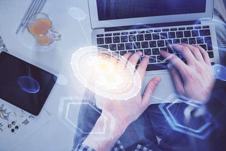 Double exposure of man's hands typing over computer keyboard and crypto currency theme hologram...