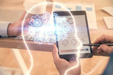 Double exposure of man's hand holding and using a digital device and brain hologram drawing. Data...