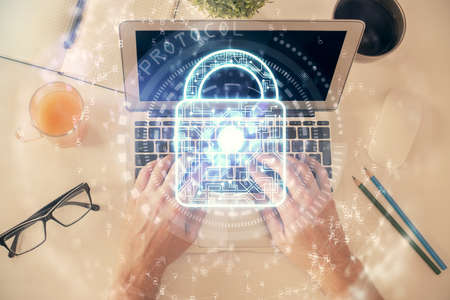 Multi exposure of man's hands typing over computer keyboard and lock hologram drawing. Top view....