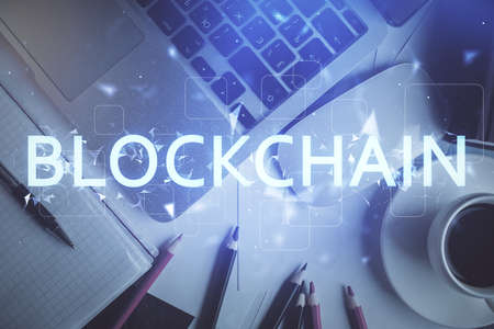 Blockchain theme hologram drawings over computer on the desktop background. Top view. Multi...