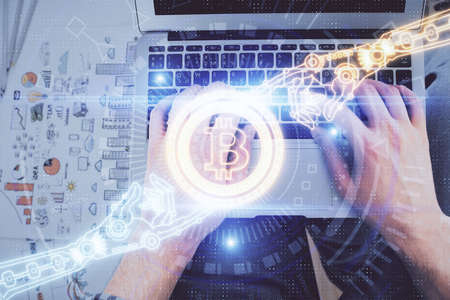 Double exposure of man's hands typing over computer keyboard and crypto currency theme hologram...