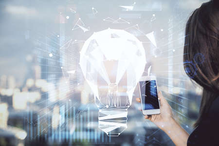 Double exposure of light bulb hologram and woman holding and using a mobile device. Idea concept.