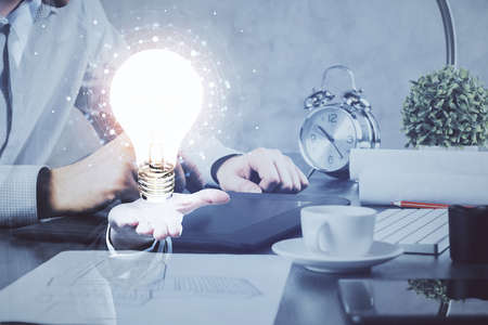 Double exposure of man's hands holding and using a digital device and bulb hologram drawing. Idea...