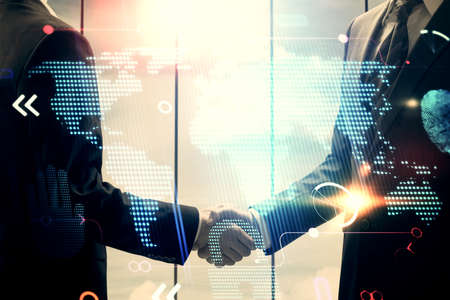 Double exposure of world map hologram and handshake of two men. International partnership concept.