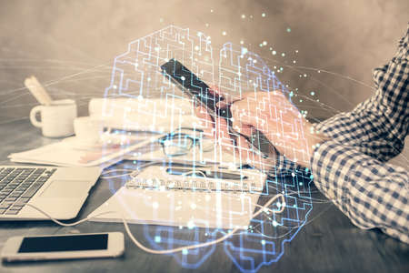 Double exposure of man's hand holding and using a digital device and brain hologram drawing. Data...