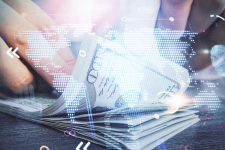 Double exposure of world map drawing hologram and us dollars bills and man hands.