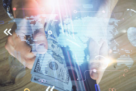 Double exposure of world map drawing hologram and us dollars bills and man hands.