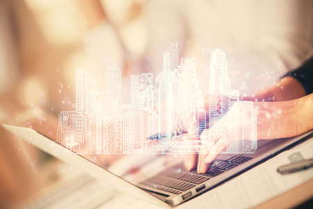 Double exposure of woman hands typing on computer and buildings drawing. Smart-city concept.の写真素材