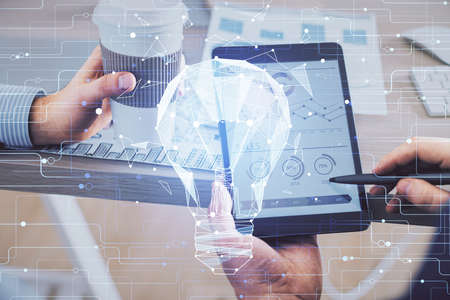 Double exposure of man's hands holding and using a digital device and bulb hologram drawing. Idea...
