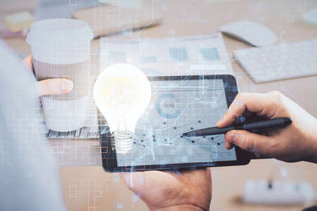 Double exposure of man's hands holding and using a digital device and bulb hologram drawing. Idea...