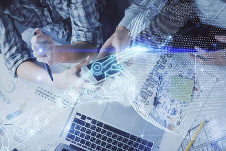 Double exposure of tech theme hologram and man and woman working together holding and using a mobile device.の写真素材