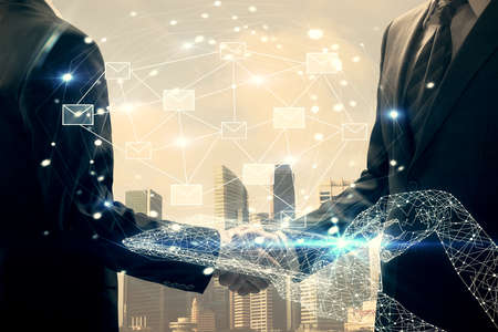 Double exposure of envelop flying in air drawing hologram and handshake of two men. E-mail concept.の写真素材