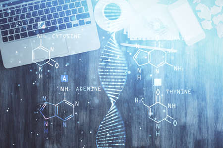 DNA hologram drawings over computer on the desktop background. Top view. Multi exposure. Concept...