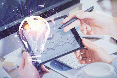 Double exposure of man's hands holding and using a digital device and bulb hologram drawing. Idea...