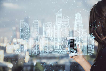 Double exposure of buildings hologram and woman holding and using a mobile device. Smart city...